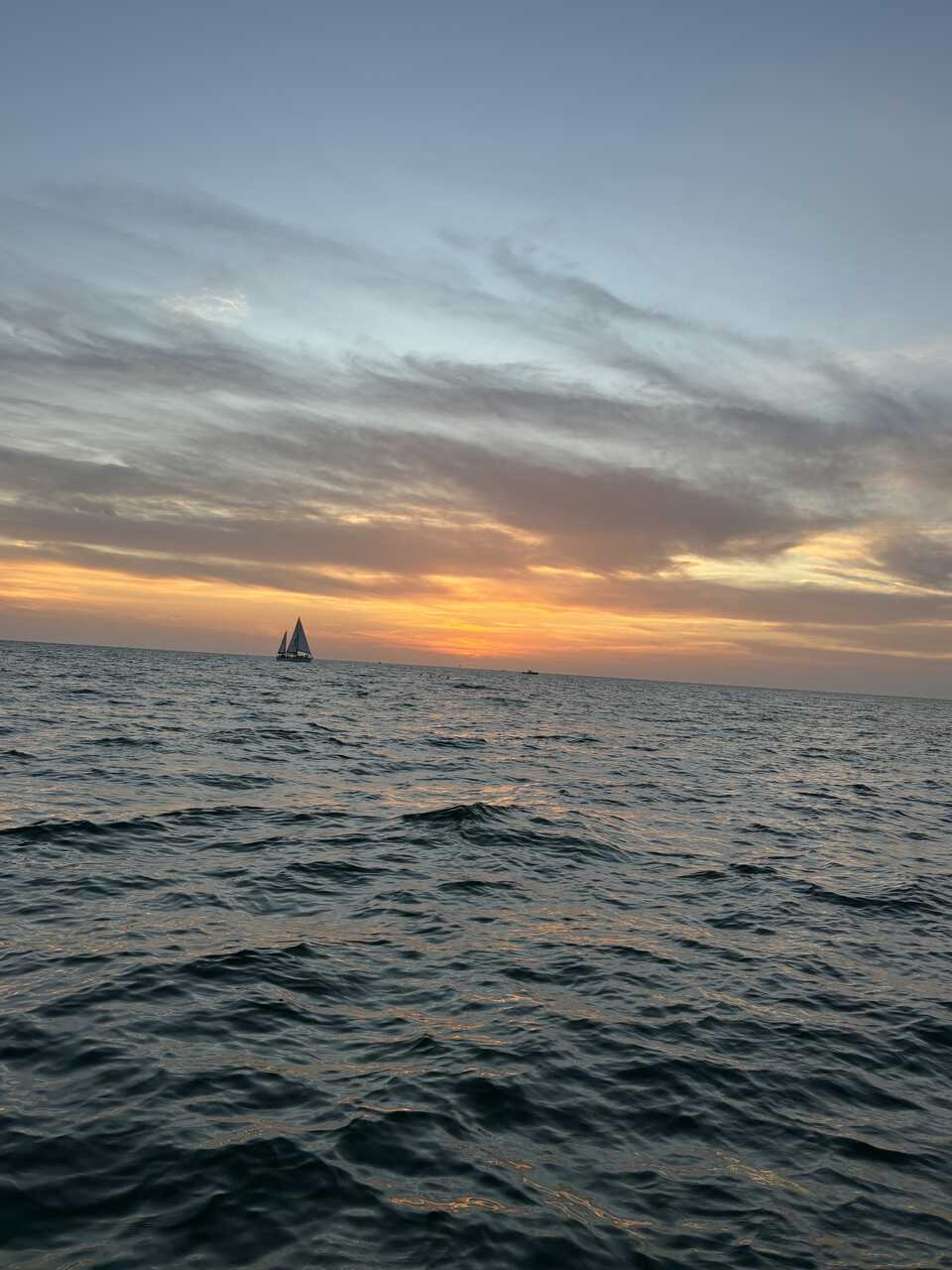 A sailor with St. Pete Sun Cruise sails toward the horizon during sunset.